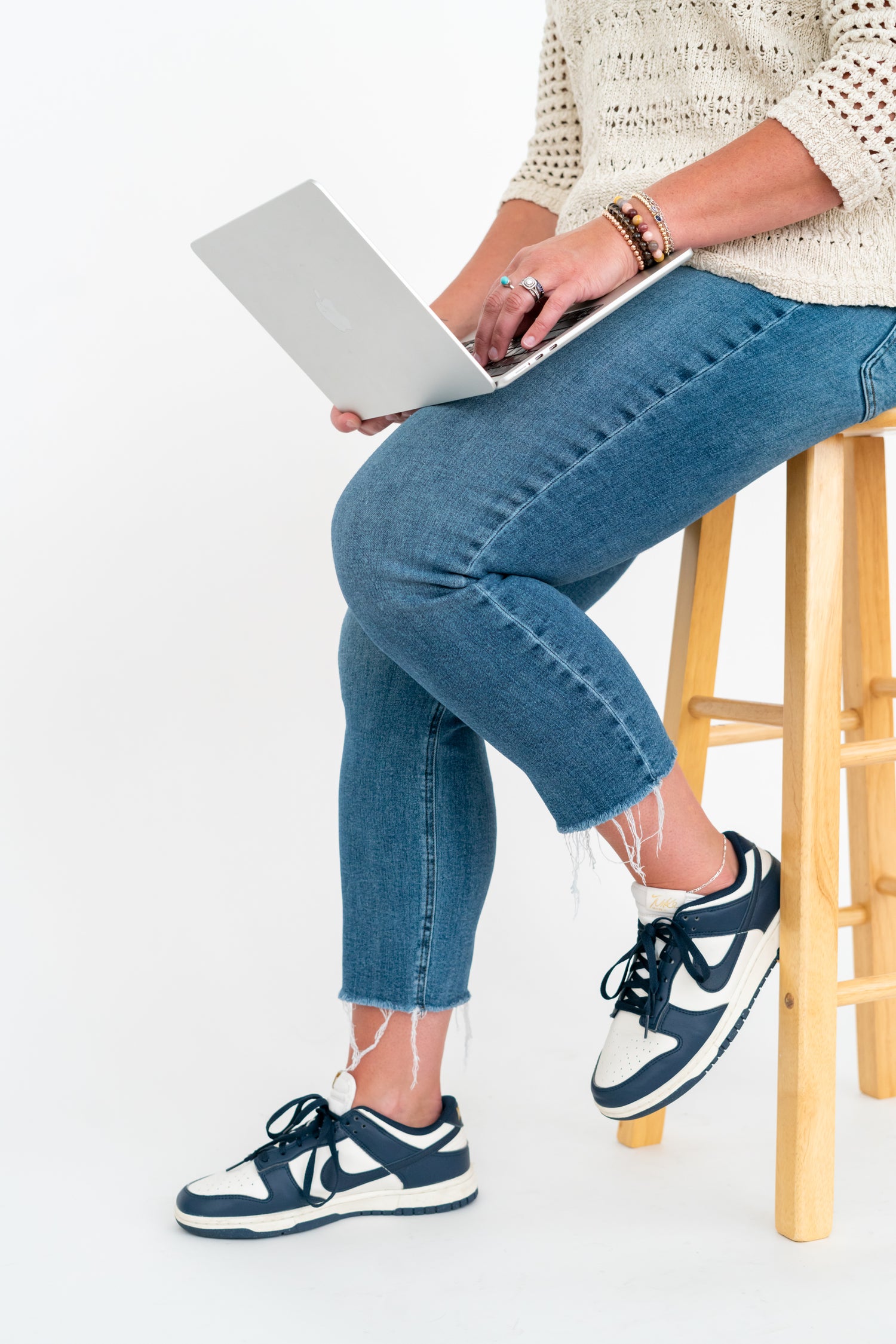 Person sitting on a stool using a laptop, wearing blue jeans and navy sneakers.