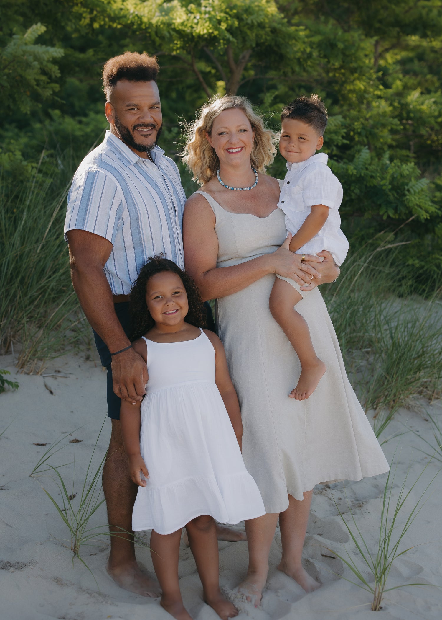 Owners family of four standing on a sandy beach with greenery in the background